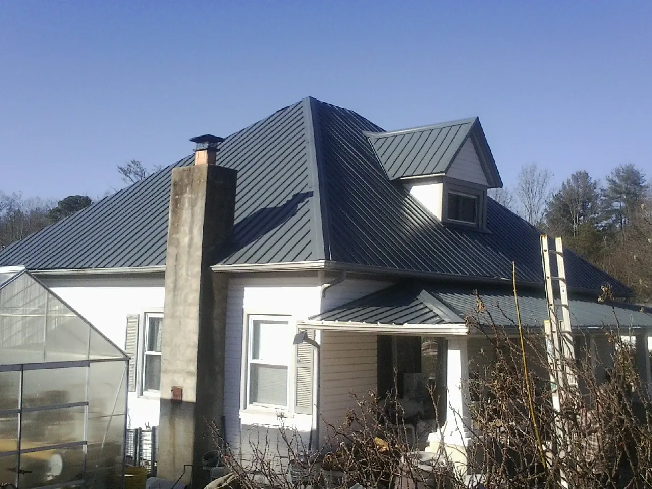 Dark blue standing seam metal roof on a white farmhouse with dormer — Slate & Tile Roof Repair by Roofing Brothers in Mcdonough