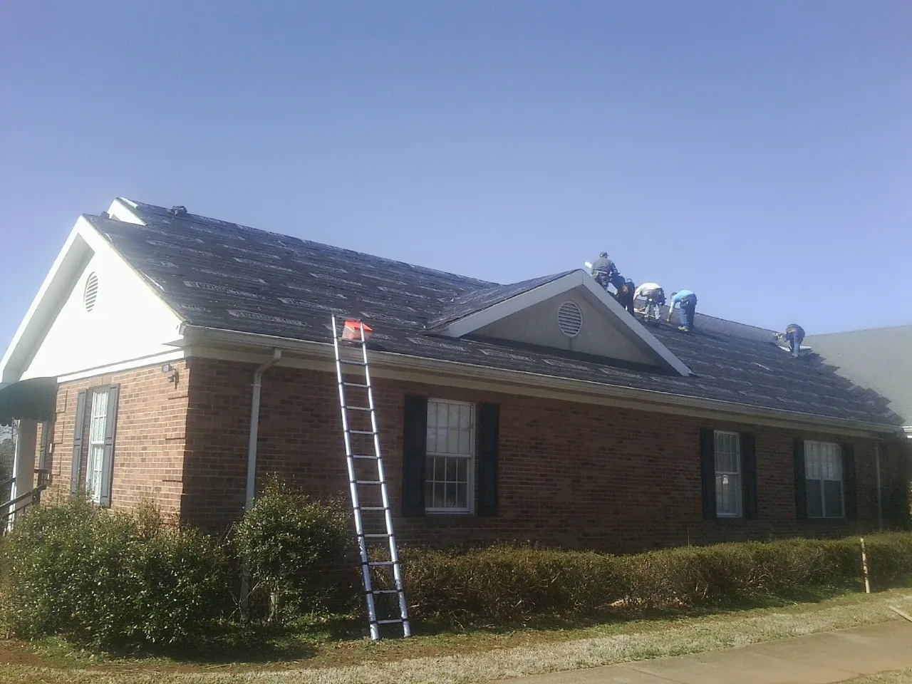 Crew tearing shingles off a brick ranch roof with a ladder set — Emergency Roof Repair work by our crew in Mcdonough