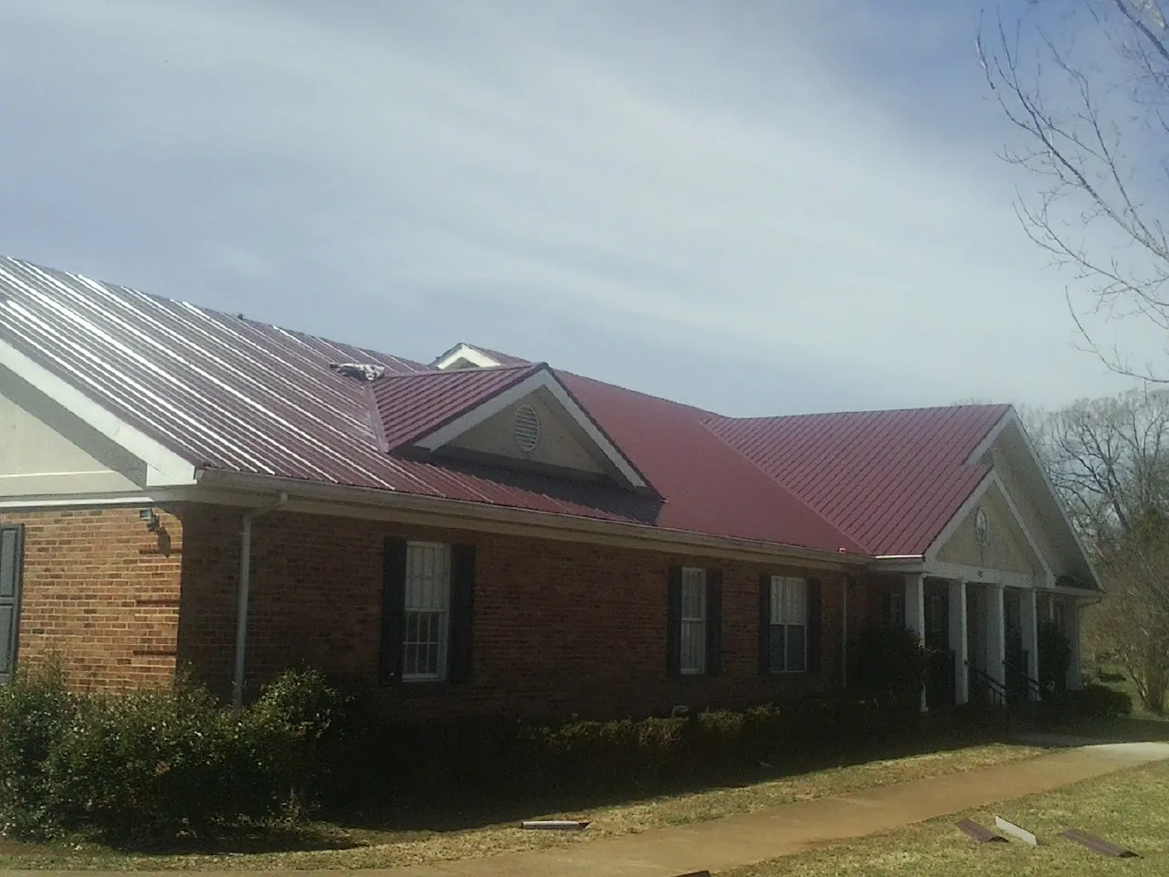 Red metal roof with gabled entries on a long brick building, from a Hail Damage Roof Repair job in Mcdonough