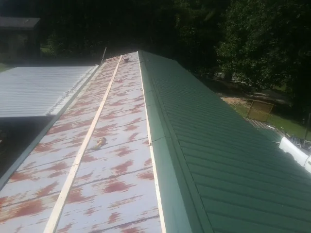 Old rusted panels beside newly installed green metal roofing — Wind Damage Roof Repair by Roofing Brothers in Mcdonough