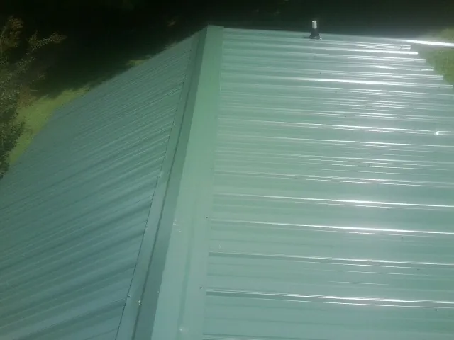 New green metal panels meeting at the ridge of a roof — Flat Roof Repair work by our crew in Mcdonough