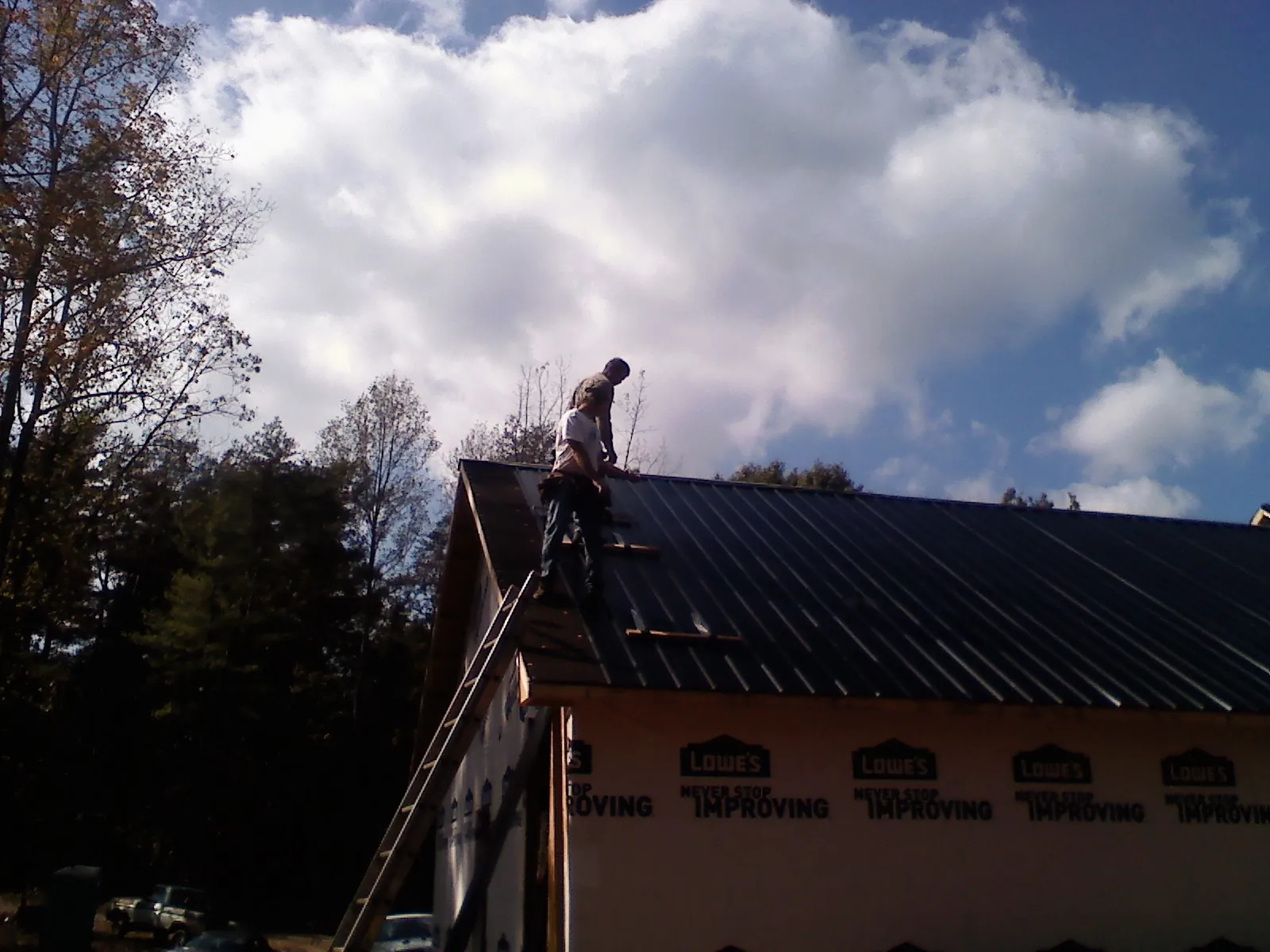 Roofer fastening dark metal panels high against a cloudy sky, from a Roof Inspection job in Mcdonough