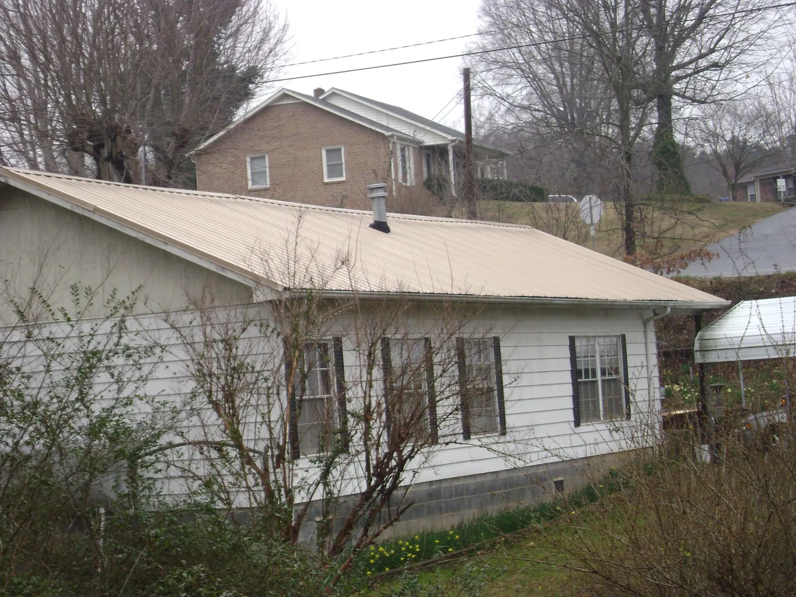 Tan metal roof on a white sided house set into a hillside — Commercial Roofing by Roofing Brothers in Mcdonough