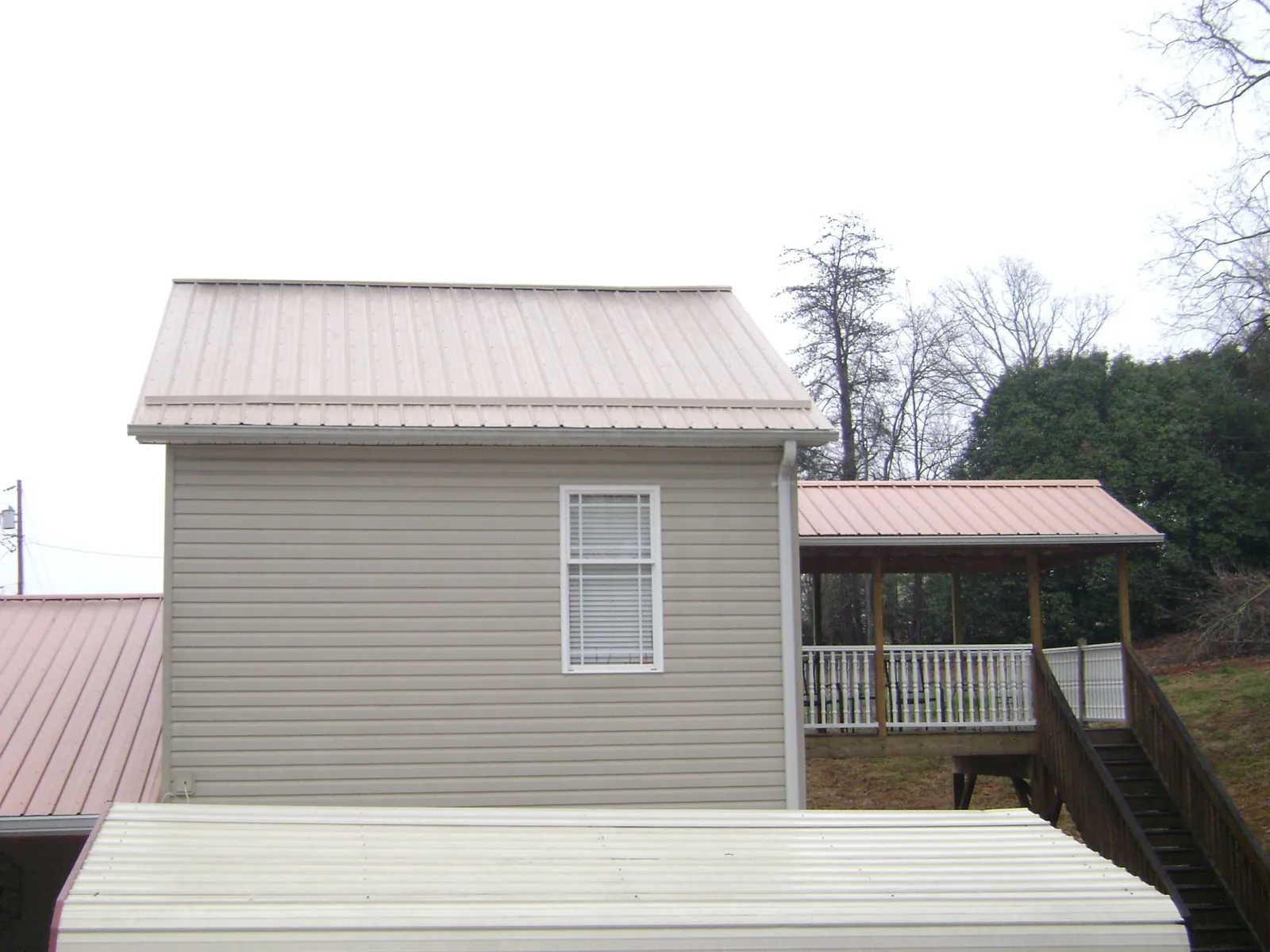 Tan metal roofs on a two story addition and attached porch, from a Roof Replacement job in Mcdonough